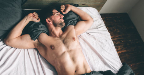 Mężczyzna bez koszulki przeciąga się w łóżku